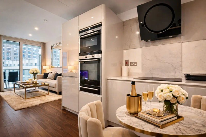 Modern open-plan kitchen and living area with marble counters, cream cabinetry, and contemporary furnishings