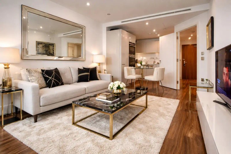 Modern living room with cream sofa, glass coffee table, mirror, and open-plan kitchen area