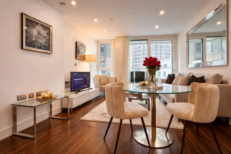 Modern living room with round dining table, upholstered chairs, TV, and large windows