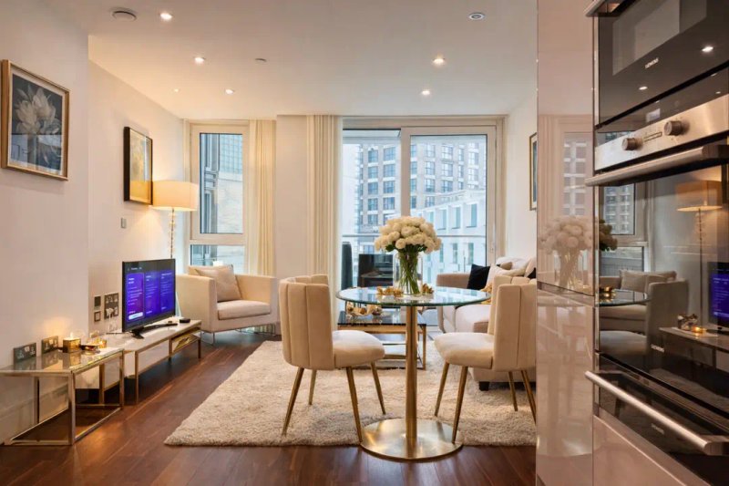 Modern open-plan living and dining area with cream furniture, dining table, kitchen, and city views