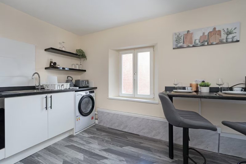 Modern kitchen with white cabinetry, washing machine, black countertops and dining area