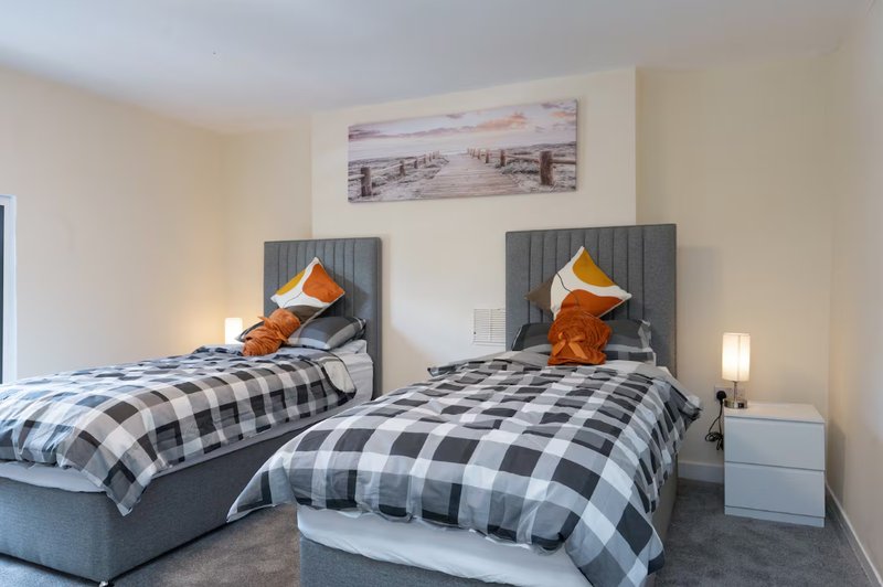 Twin bedroom with checkered bedding, orange cushions, wooden headboards and wall art