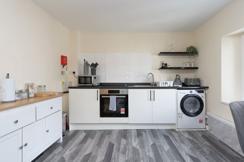 Modern kitchen with white units, black countertop, integrated oven, washing machine and shelving