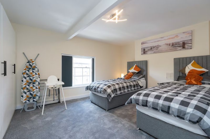 Bright twin bedroom with two beds, checkered bedding, ironing board and window