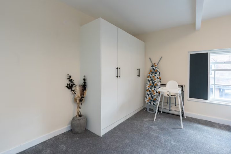 Modern bedroom with white built-in wardrobe, grey flooring, and minimalist decor including dried flowers