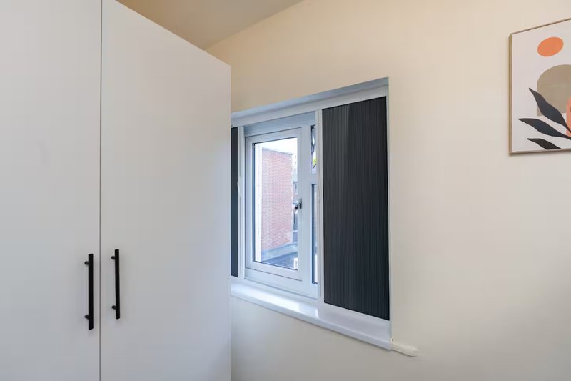 Modern bedroom with white built-in wardrobe, window with black blinds and abstract wall art
