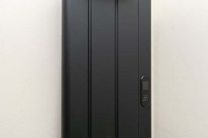 Black vertical radiator mounted on white wall with digital display panel