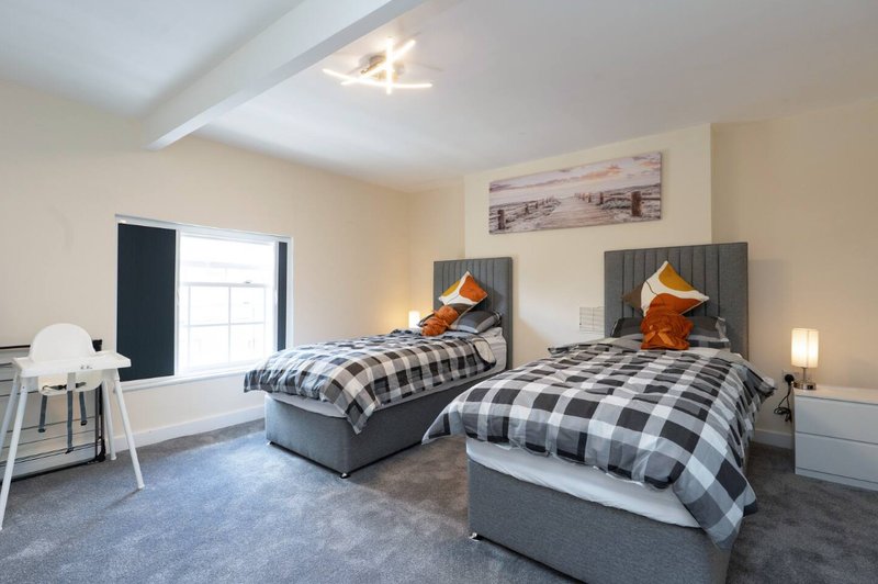 Bright twin bedroom with two single beds, grey headboards, checkered bedding and bedside lamps