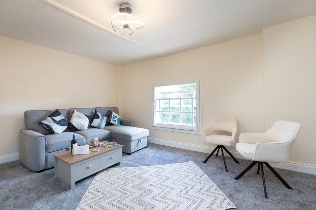 Bright living room with grey sectional sofa, white armchairs, wooden coffee table and large window