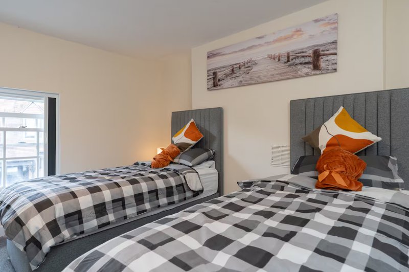 Twin bedroom with checkered bedding, gray upholstered headboards, orange pillows, and window