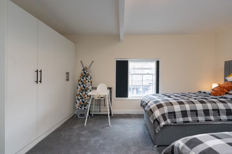 Bright bedroom with two beds, white wardrobe, desk chair and window with black frame