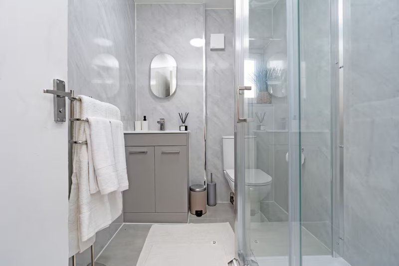 Modern bathroom with grey vanity, mirror, shower enclosure and white towels