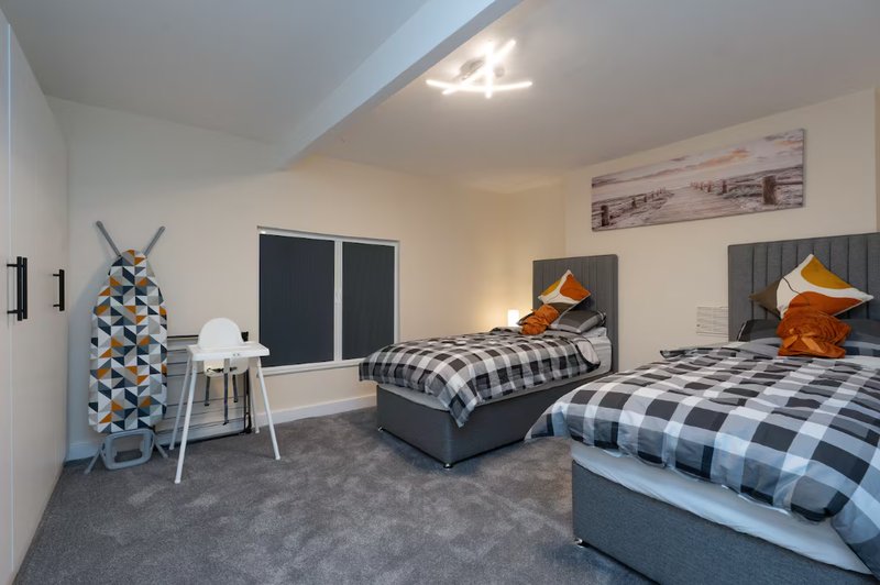 Spacious bedroom with two double beds, grey carpet, modern furnishings and artwork