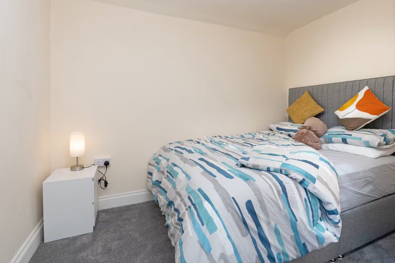 Bedroom with double bed, striped bedding, grey headboard, bedside lamp and white nightstand