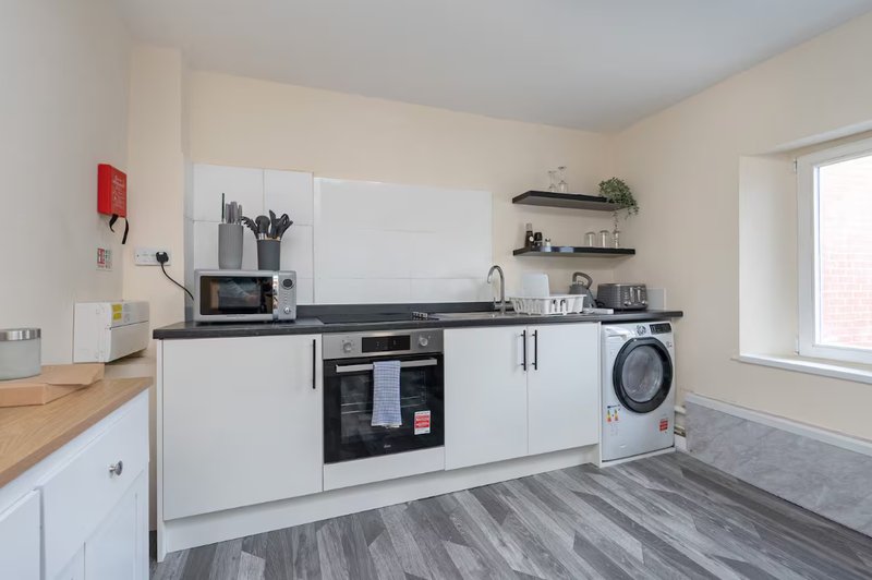 Modern kitchen with white cabinetry, black countertop, integrated oven, washing machine and window