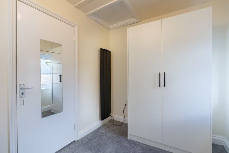 Modern bedroom with white fitted wardrobes, white door with glass panel, and grey carpet flooring