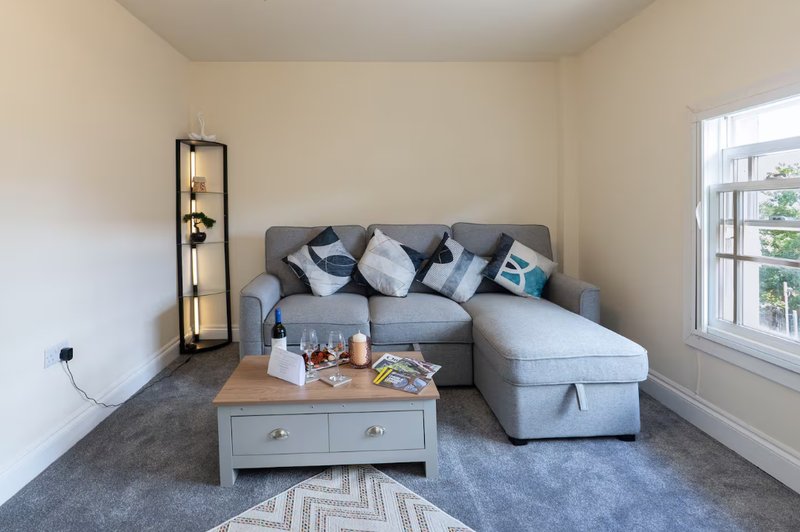 Modern living room with grey corner sofa, wooden coffee table, floor lamp and window with natural light