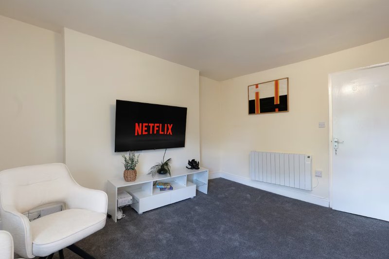 Living room with TV on wall, white armchair, white TV stand, and dark grey carpet