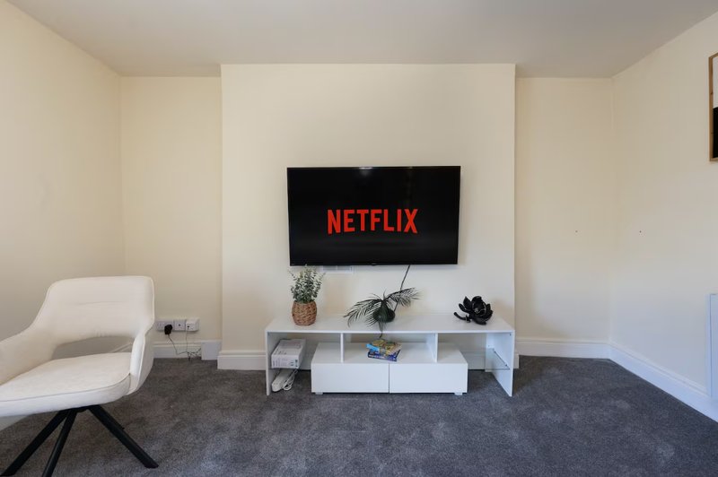 Living room with white TV stand, wall-mounted screen, white armchair and potted plants