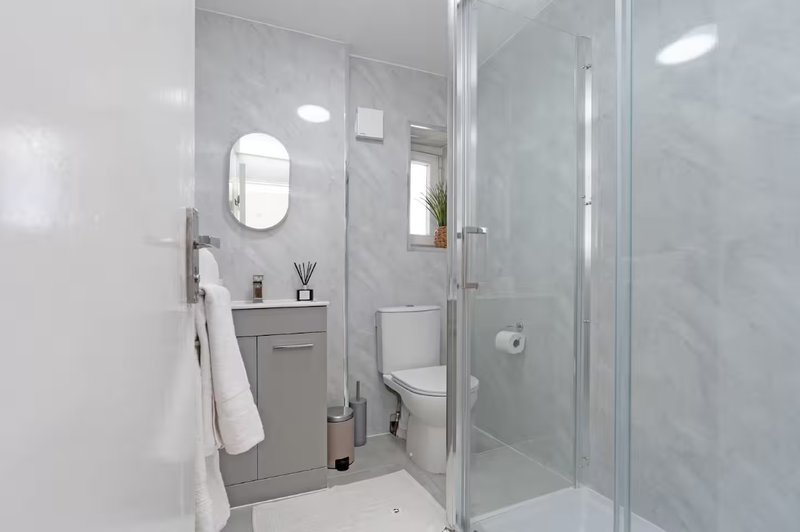 Modern bathroom with grey vanity, oval mirror, toilet, and glass shower enclosure