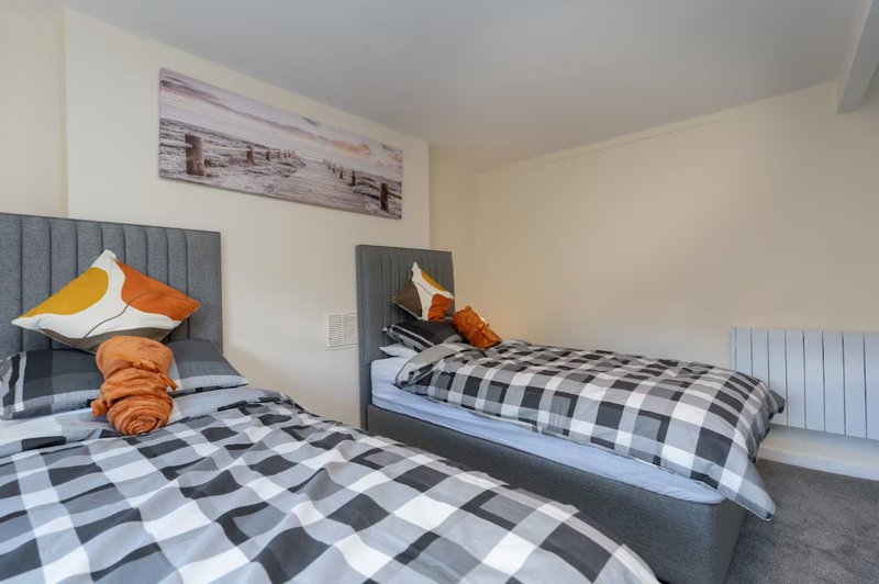 Bedroom with two single beds, checkered bedding, orange cushions and wall art