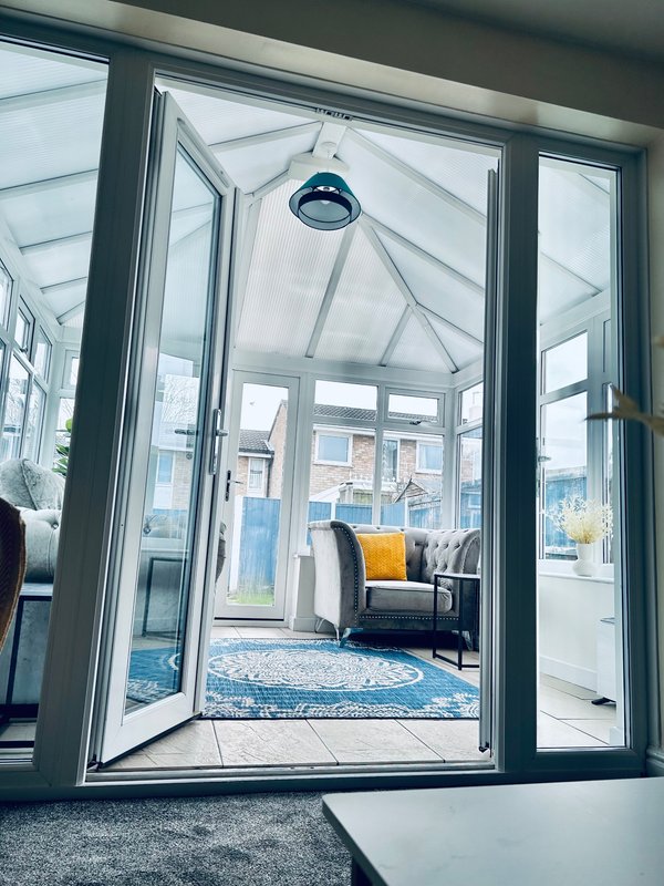 Modern conservatory with glass doors, blue rug, armchair and pendant light overhead