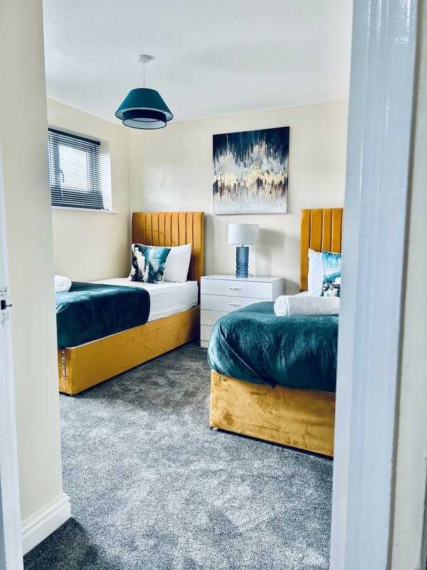 Modern bedroom with two single beds with golden upholstered frames, white bedside table, blue pendant light and wall art