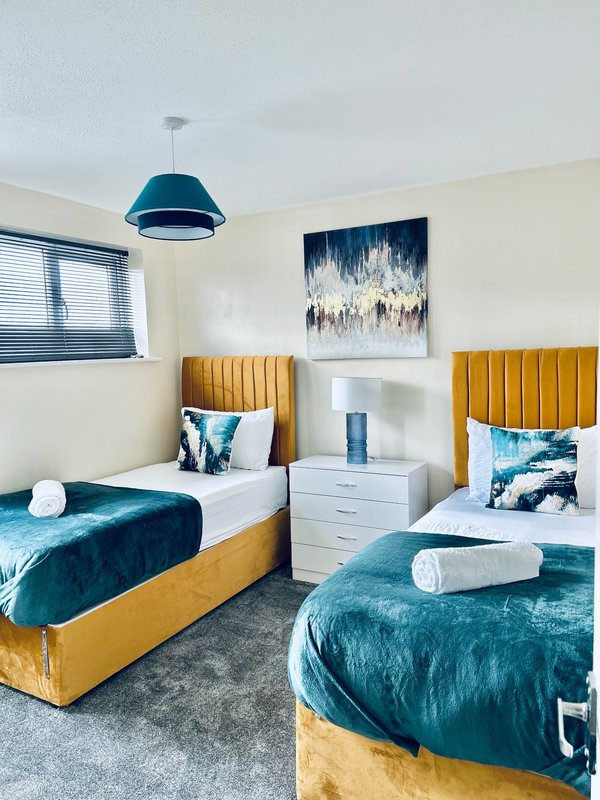 Twin bedroom with teal velvet beds, gold headboards, shared nightstand and pendant light