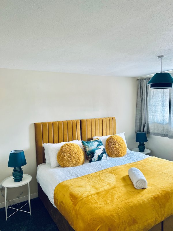 Modern bedroom with mustard velvet headboard, yellow bedding, decorative cushions and pendant light