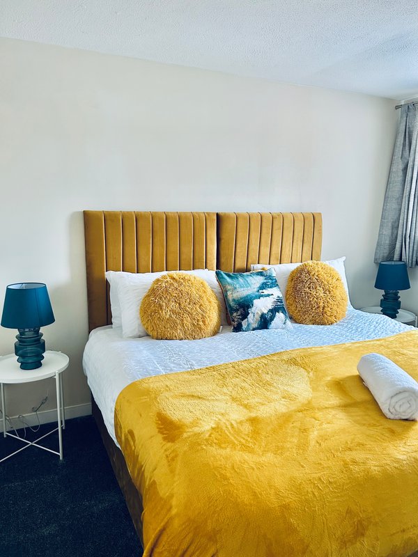 Modern bedroom with gold velvet headboard, yellow bedding, and decorative cushions