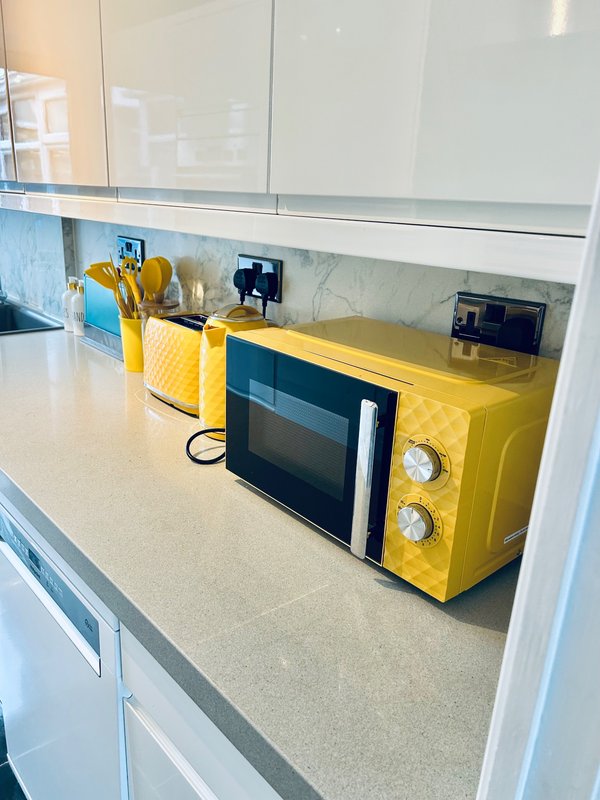 Modern kitchen counter with yellow microwave, utensil holder, and white cabinetry