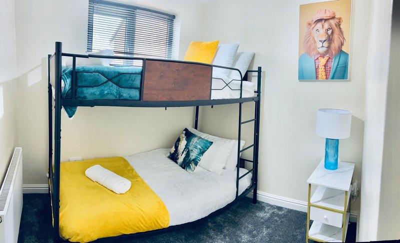 Bedroom with black metal bunk bed, yellow bedding, blue cushions and wall art