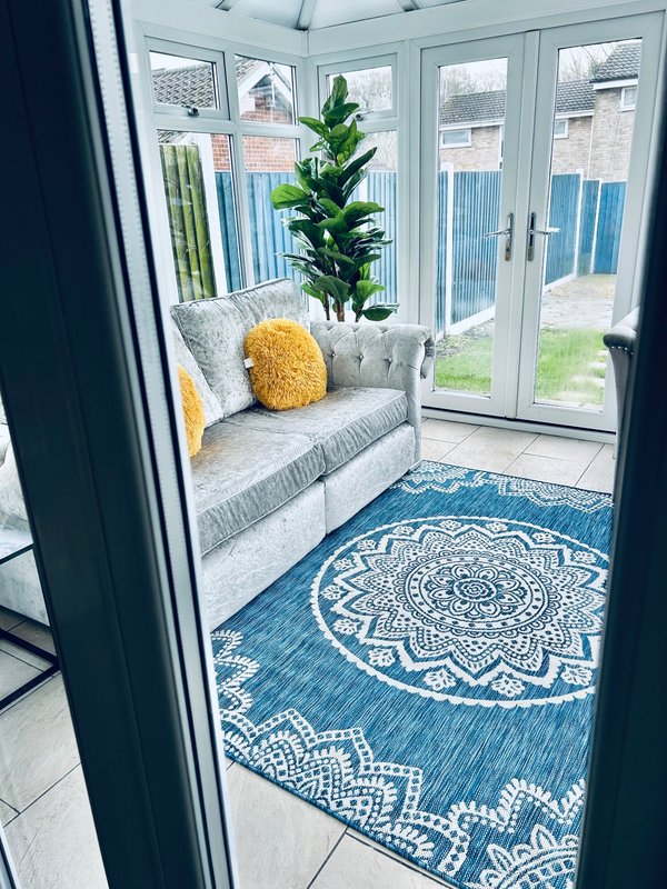 Bright conservatory with grey seating, patterned blue rug, potted plant, and glass doors to garden