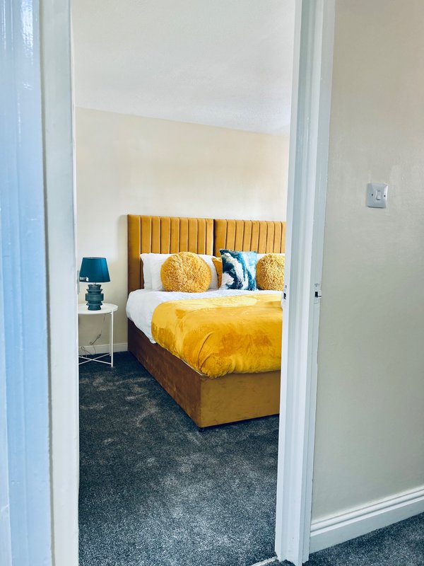 Modern bedroom with gold velvet bed, yellow bedding, decorative pillows and bedside lamp
