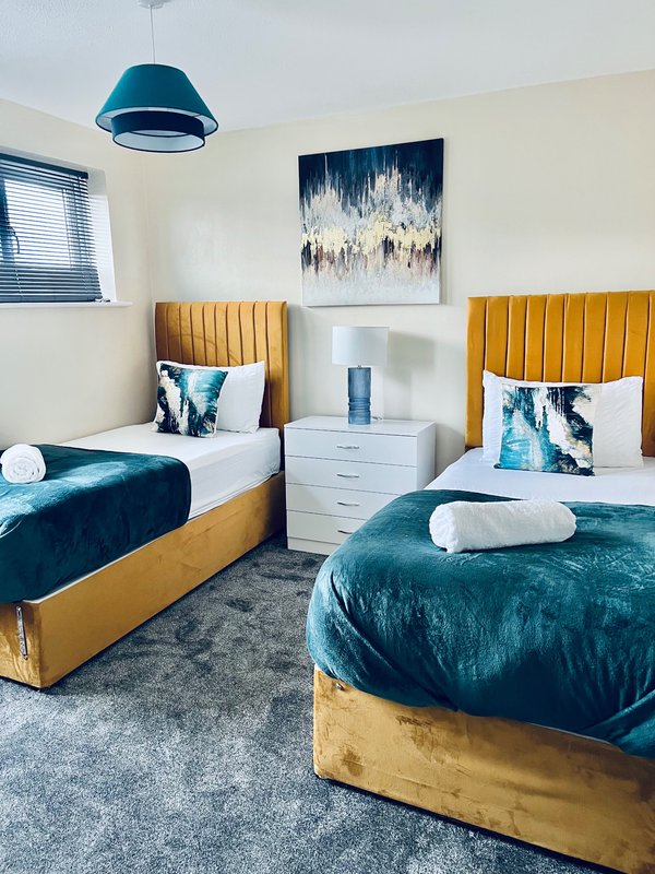 Modern twin bedroom with gold headboards, teal bedding, blue pendant light and abstract wall art