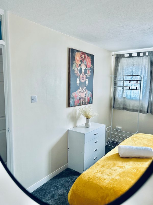 Bedroom with yellow bench, white dresser, framed artwork, and window with curtains