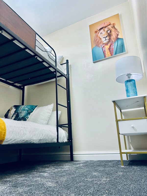 Bedroom with black metal-frame bed, blue lamp, wall art, and side table with shelving
