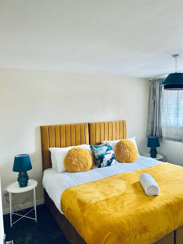 Modern bedroom with yellow upholstered headboard, white bedding, yellow throw, and teal pendant light