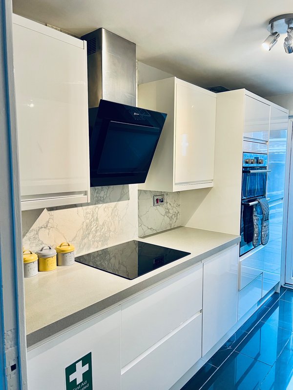 Modern white kitchen with black cooktop, marble splashback, black extractor hood and yellow storage jars