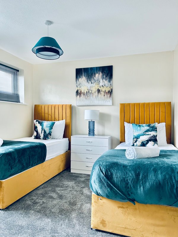 Modern bedroom with two single beds, gold headboards, teal bedding, and blue pendant light