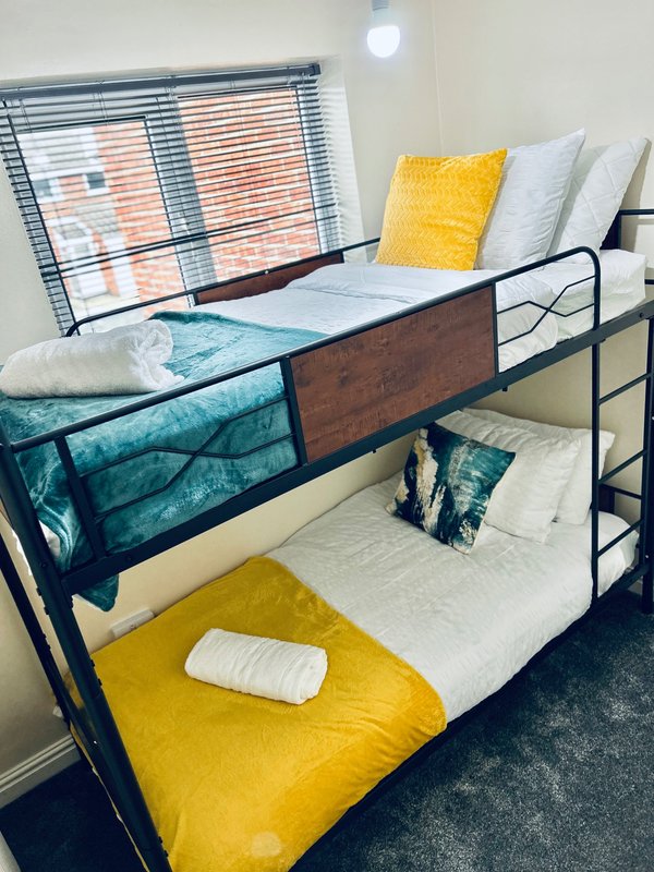 Dormitory-style bunk bed with yellow and teal bedding, pillows, and metal frame