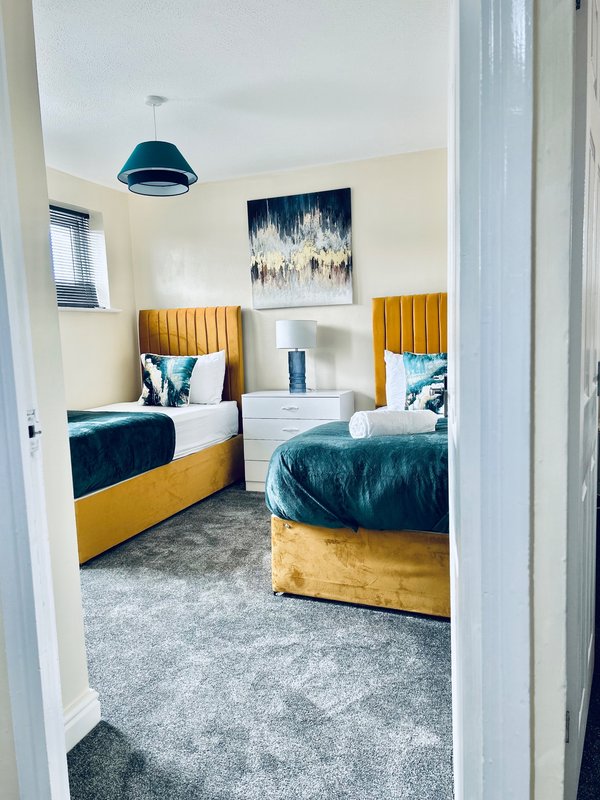 Twin bedroom with gold upholstered beds, white bedside table, blue pendant light and artwork