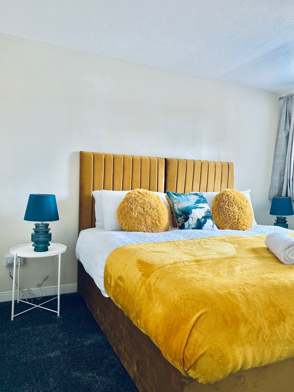 Modern bedroom with yellow upholstered headboard, gold bedding, decorative cushions and side lamps