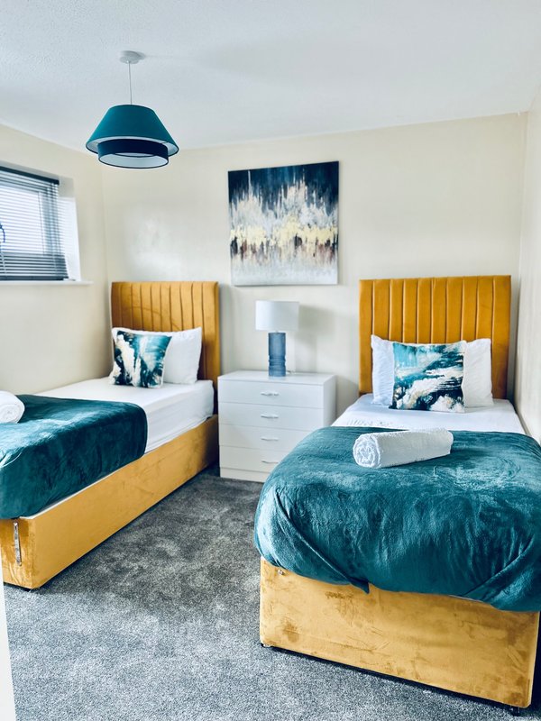 Twin bedroom with yellow upholstered beds, teal bedding, pendant light, and abstract wall art