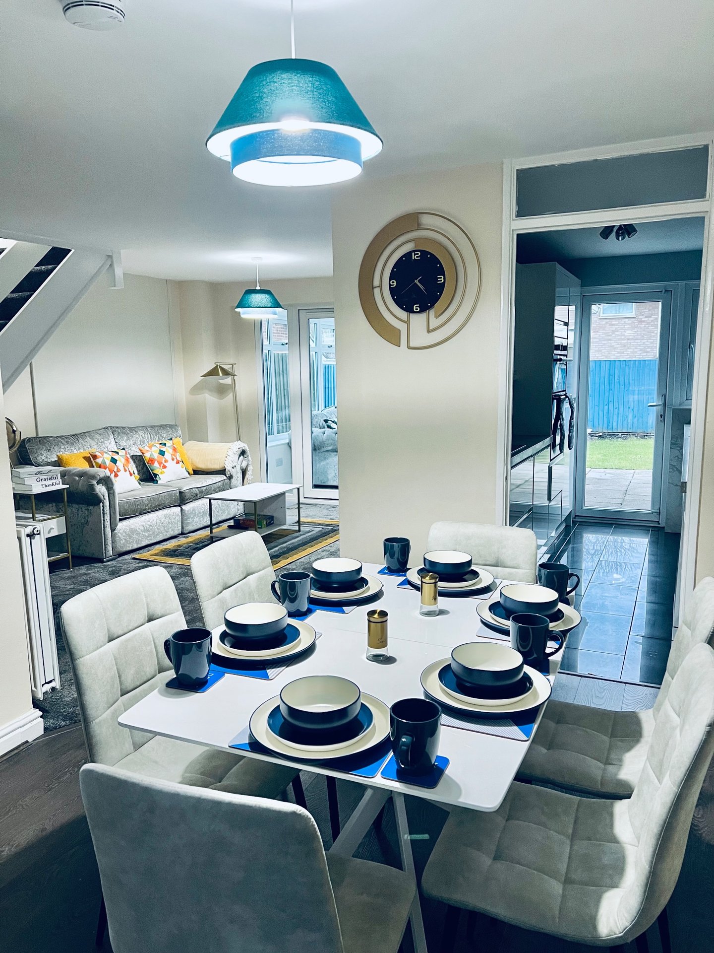 Modern open-plan dining and living area with white table, blue pendant light and grey sofa