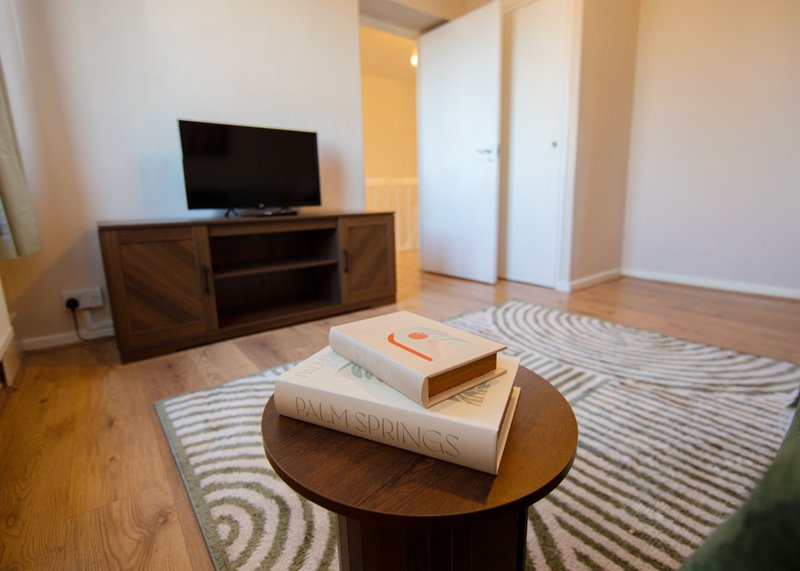 Spacious living room with wooden furniture, TV stand, round coffee table, striped rug and white doors