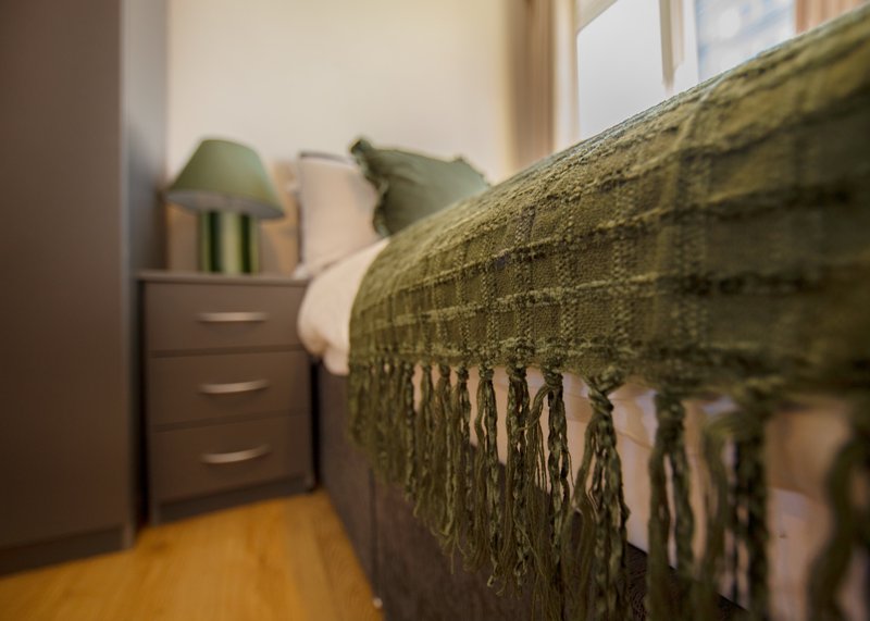 Bedroom with wooden floor, dresser, green bedding and decorative throw blanket
