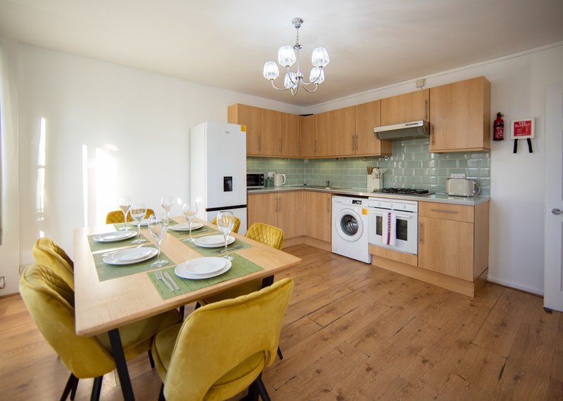 Modern kitchen-diner with wooden cabinets, dining table, yellow chairs and appliances