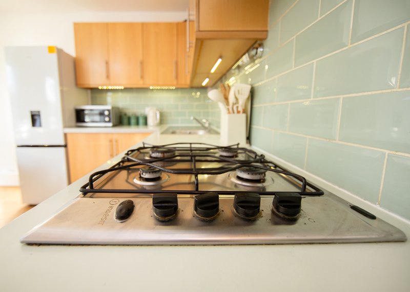 Kitchen with gas hob, green tile backsplash, wooden cabinets and white appliances