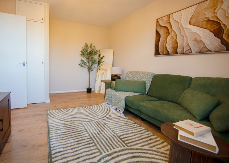 Bright living room with green sofa, patterned rugs, wooden floor and wall art